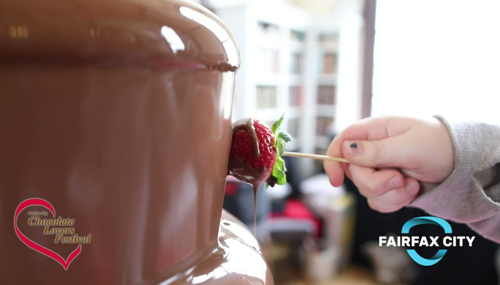 Image of a hand holding a strawberry on a stick, putting it into a chocolate fountain