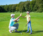 Image of a dad and son high fiving on the golf course while wearing golf gear, harts and holding a club