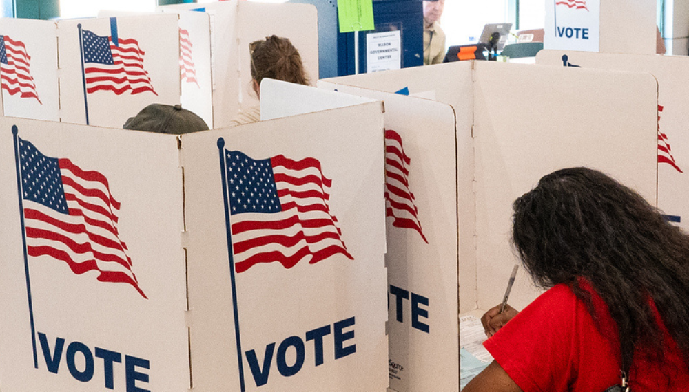 Image of people voting behind dividers with the text "VOTE" and a graphic of the American flag
