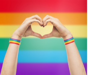 Image of hands making a heart in front of a Pride flag backdrop