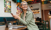 Photo of a smiling older woman in a coffee shop holding a smartphone.