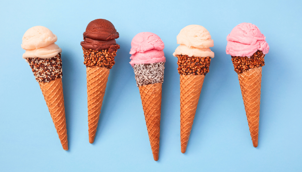 Image of chocolate, vanilla and strawberry scoops of ice cream on sugar cone, laying on a blue background.