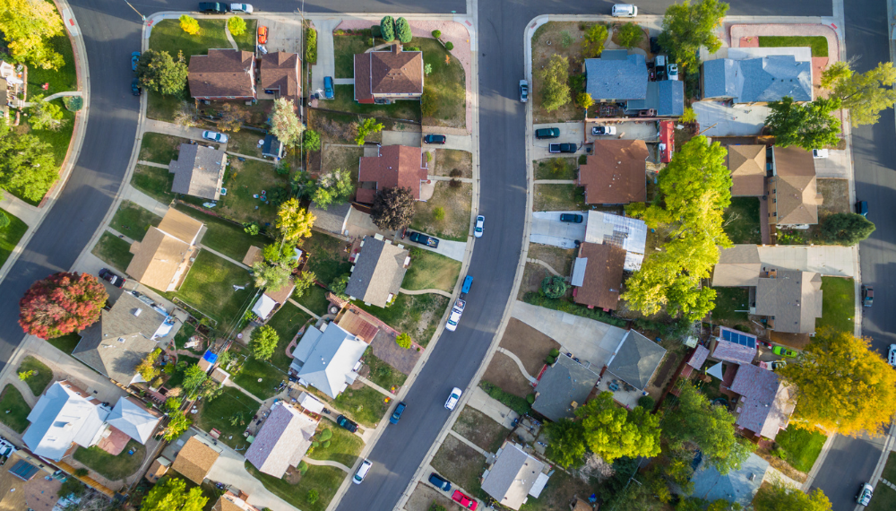 Aerial view of a neighborhood with houses, green grass and cars in driveways