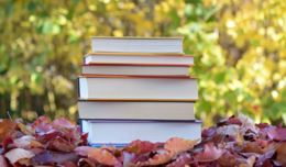 Image of a stack of books placed in a pile of fall leaves.