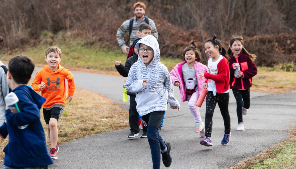 Image of kids wearing winter clothes, smiling and laughing while running outside. 