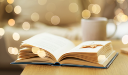 Image of a book open on a table with fairylights and a mug in the background.