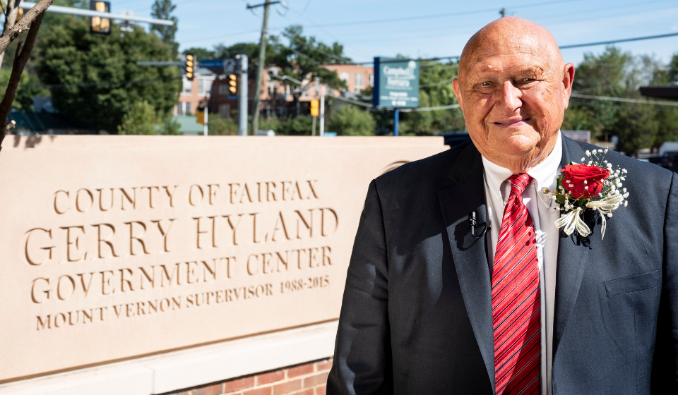 Image of former Mount Vernon District representative Gerry Highland standing in front of the Gerry Hyland Government Center sign.