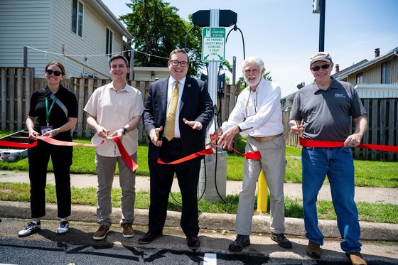 5 people in front of an EV charger cutting a red ribbon