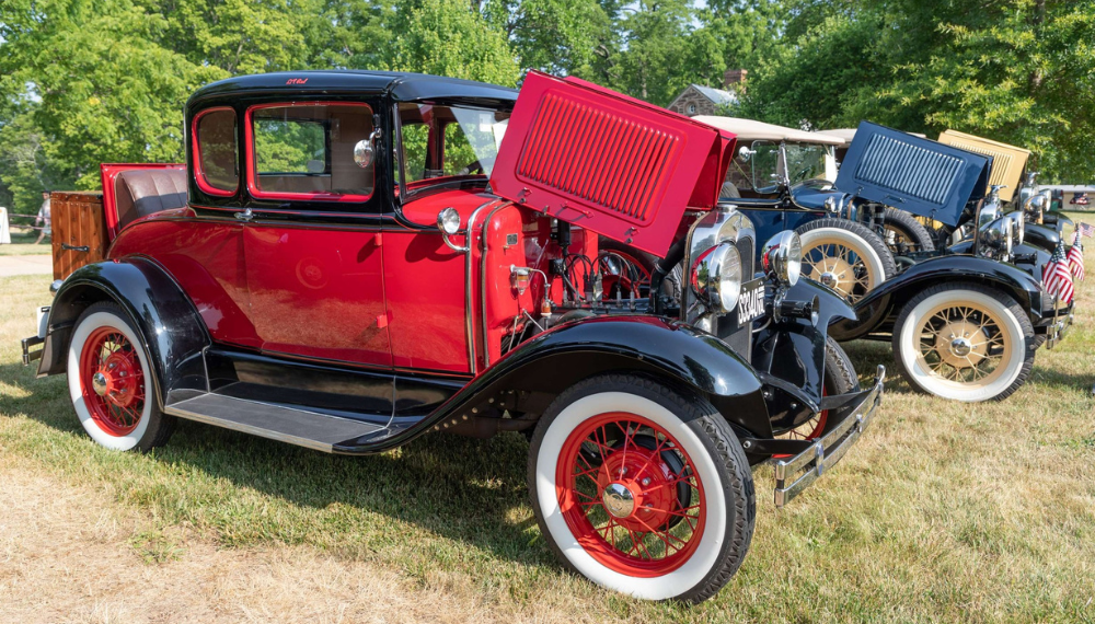 A row of colorful vintage cars is lined up on a grassy field under the sun.