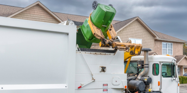trash truck with green bin in front of house