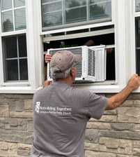 rebuilding together volunteer installing a window AC unit