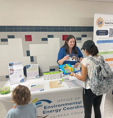 photo of woman holding a flyer talking to residents at an event table