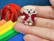Blue photo background including felt, sewing needles and yarn as elements with a open hand holding a small knit teddy bear in the foreground.