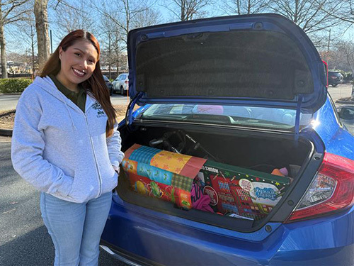 woman standing by open trunk of blue car with presents