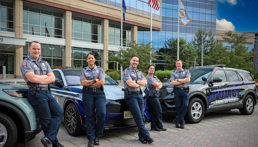 Police officers smile while posing in front of Police vehicles.