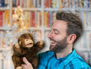 Background of library shelves with snowflake overlay, foreground features middle aged caucasian man smiling and looking at a squirrel puppet