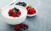 A white bowl filled with Greek yogurt and fresh berries sits on a table with smaller bowls of berries.