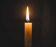 A single lit candle with a warm flame stands against a dark background.