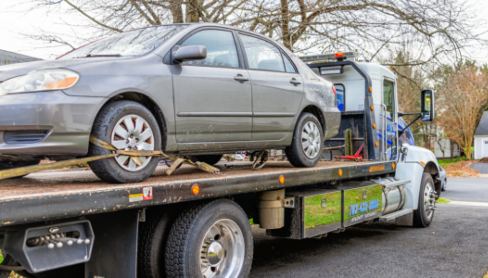 A gray car on the bed of a tow truck.