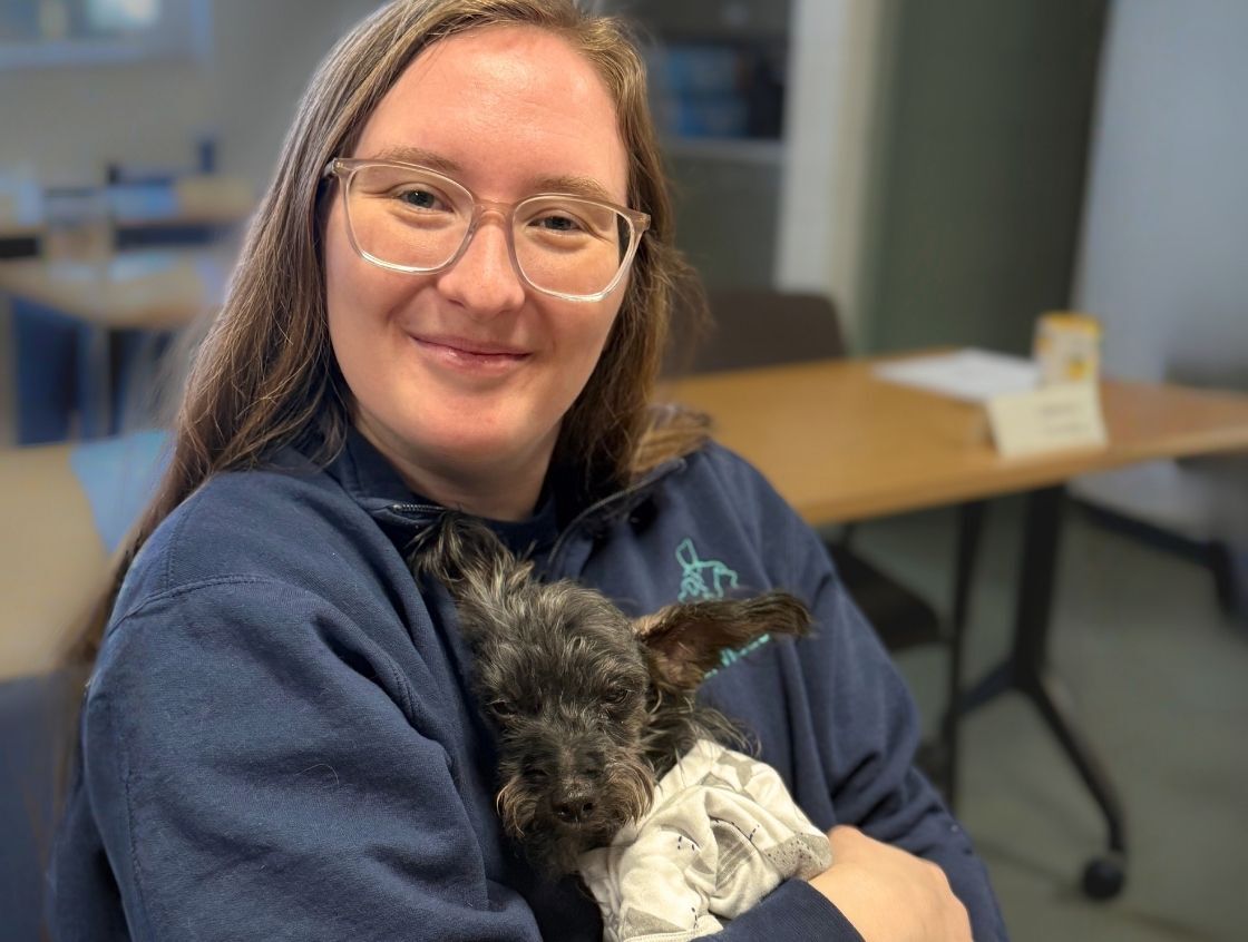 Young woman smiling holding small, sleepy dog in her arms
