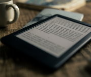 An eBook reading device next to a mug.
