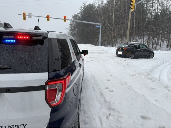 Back of a Police car in the snow with a crossover stuck in the snow in front of it. 