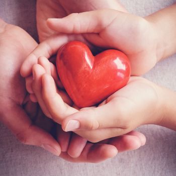 pair of hands holding a red wooden heart