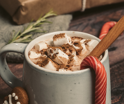 A mug of hot cocoa with a candy cane on the side of the mug.