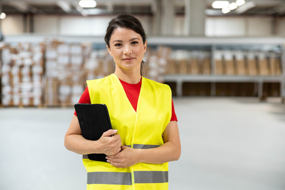 photo of woman in a warehouse wearing a high vis vest and holding a clipboard