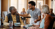 two seniors sitting at a table talking to caregiver