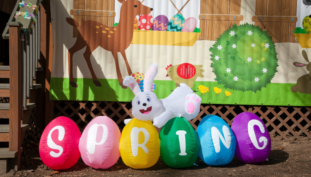 olorful inflatable eggs spelling “SPRING” with a white bunny decoration in front of a bright, cartoon-style spring backdrop.