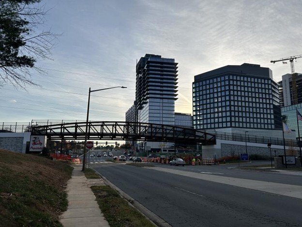 Pedestrian bridge over a multi-lane road with tall office buildings in the background.