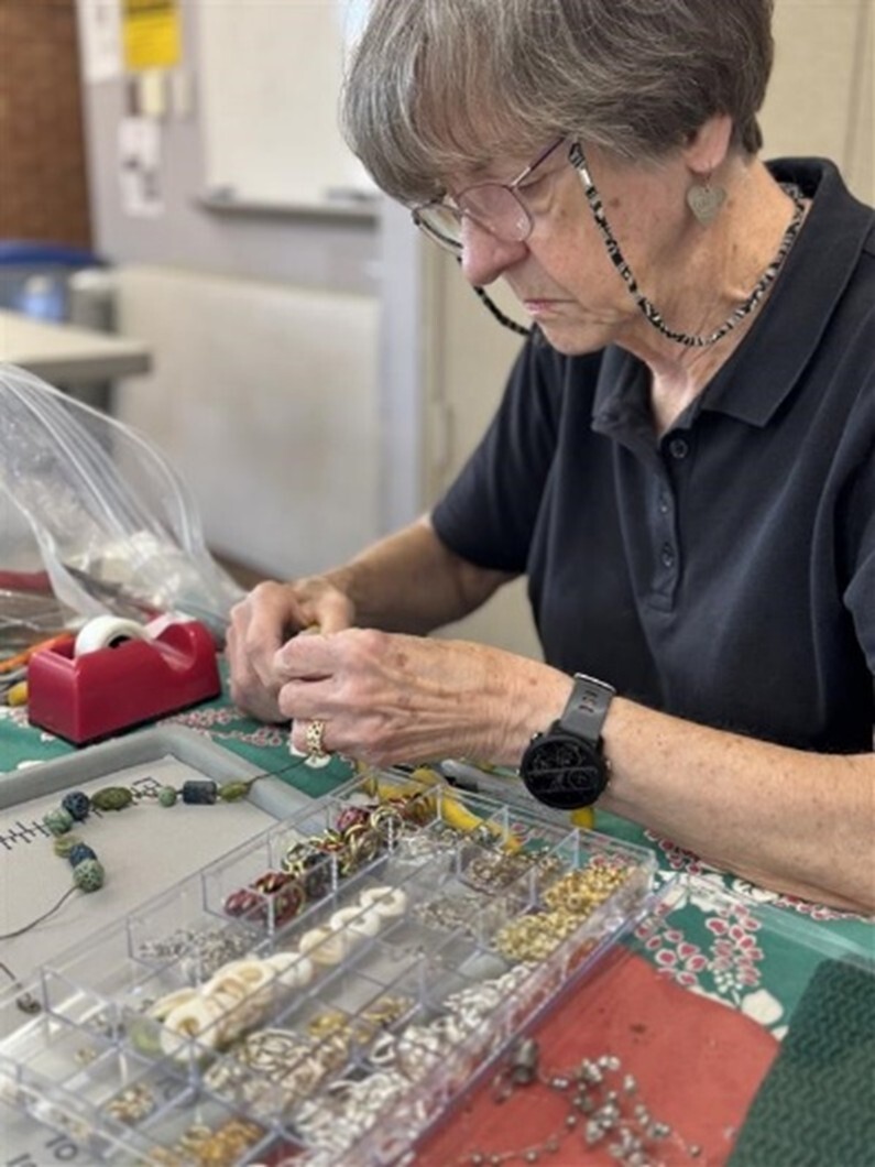 Person seated at a table sorting and assembling jewelry pieces from an organizer tray.