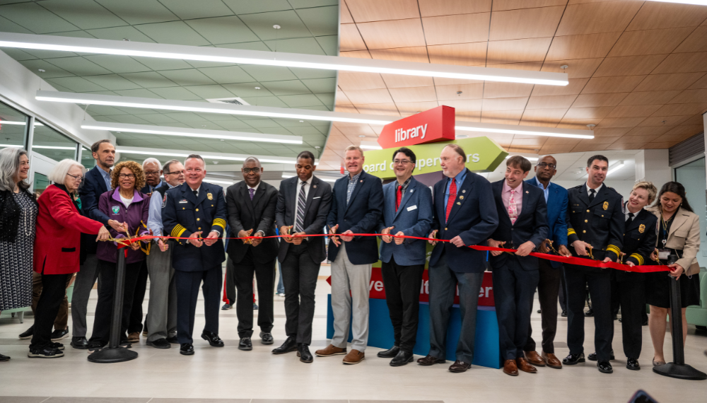 A line of board members, Fairfax County employees and the county executive hold a red ribbon in a line.