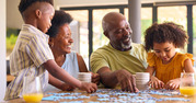 Grandparents sitting at a table with their two grandchildren putting a puzzle together.