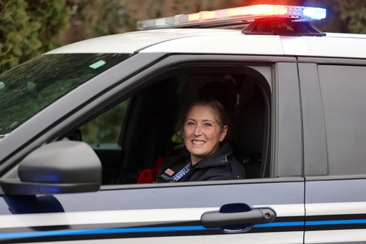 A woman smiles sitting in the drivers seat of a Police car.