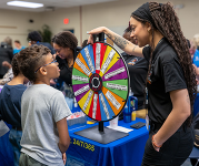 A child stands in front of a trivia wheel, trying to win a prize. 
