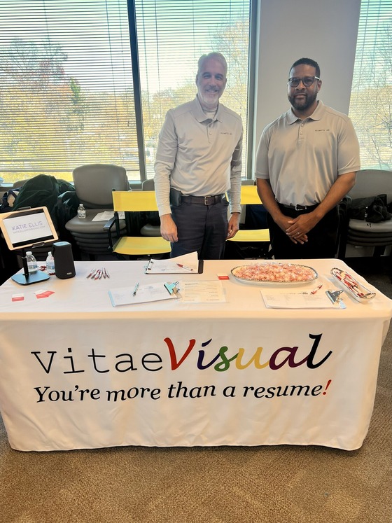 two men standing behind a table that says Vitae Visuals