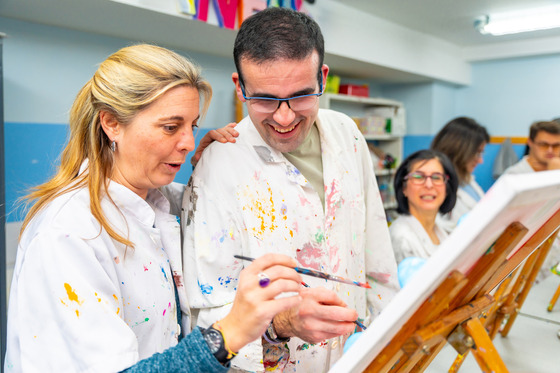 teacher helps student with developmental disabilities paint 