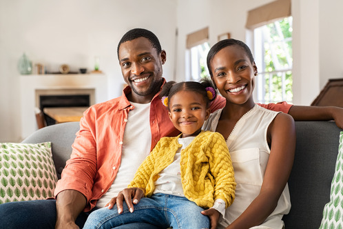 A  young family smiles sitting on a sofa.