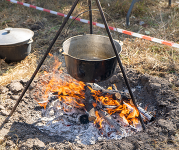 A pot hangs from a tripod over an open campfire.