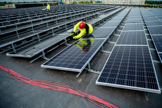 Worker in safety gear installing solar panels on a large rooftop array.