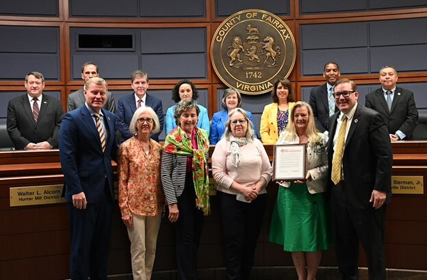 Group receiving a framed proclamation in the Fairfax County, Virginia government chamber.