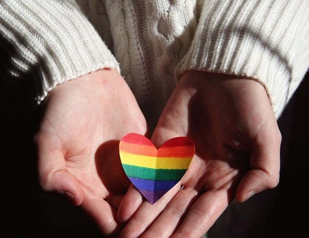A person holds a rainbow paper heart in their hands to represent Pride Month.