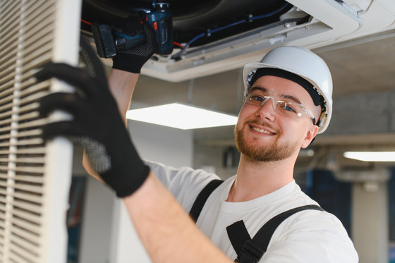 hvac technician repairing air conditioning unit with a drill