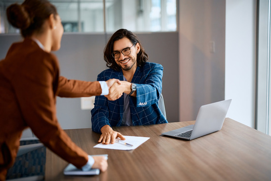 smilng man shakes hands with female colleague in office setting