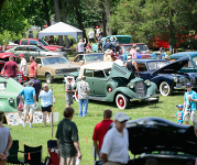 People surrounding vintage cars at a previous year's car show.