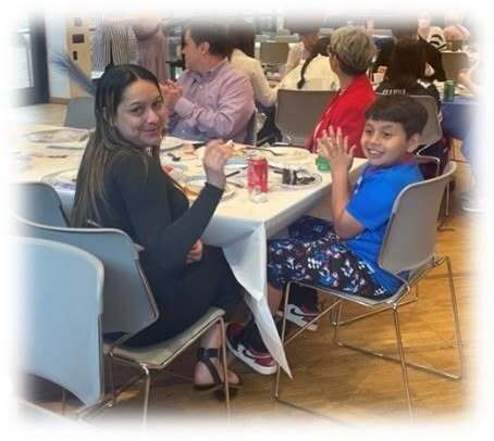 A mother and son smiling sitting in chairs at a table.