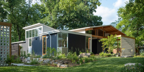 Modern home with large windows, dark siding, and natural landscaping surrounded by trees and a green lawn.