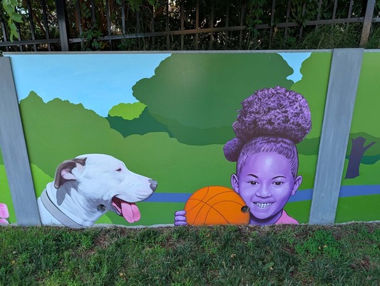 One portion of the North Hill Park mural that shows local dog Lincoln and a young girl smiling holding a basketball.